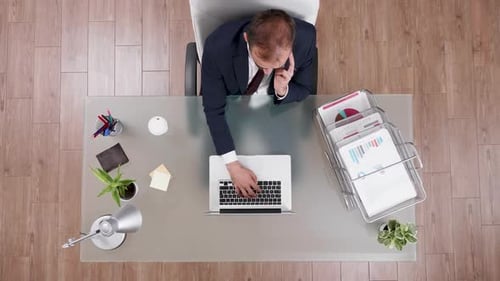 Top View of Businessman in Suit Talking on the Phone and Typing on Laptop