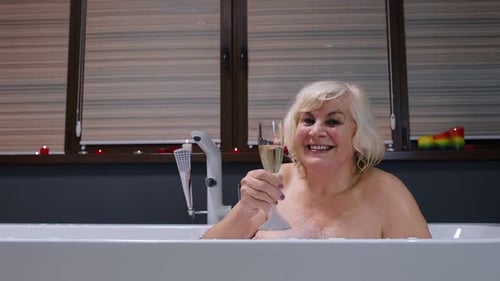Senior Woman Smiling and Celebrating in Bath with Champagne