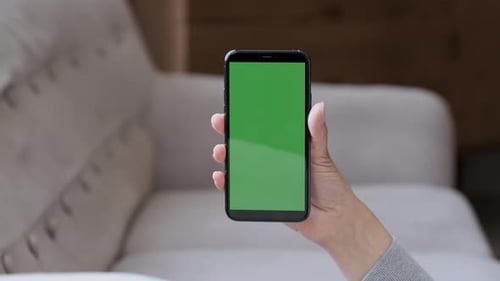 Isolated woman hands holding vertical smartphone with green mock up screen. Business woman