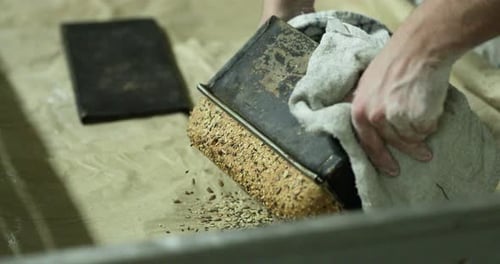 Hands Of A Baker Re Freshly Baked Loaf Bread With Sesame Seeds From A Baking Pan. - close up shot