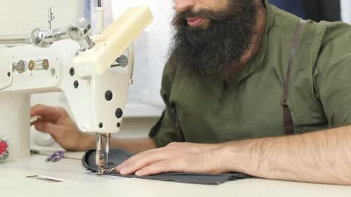 Man Sews Dark Cloth with Sewing Machine