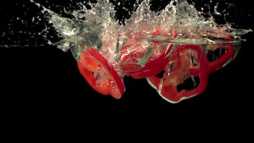 Rote Paprikastücke in Superzeitlupe fallen mit Spritzern ins Wasser