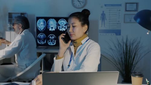 Asian Woman Doctor Talking on Mobile Phone and Looking at Lungs CT Images in Evening in Dark