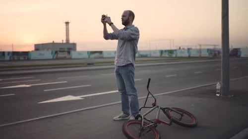 Young Man with Bmx Bicycle Uses His Phone at Sunset on the Street