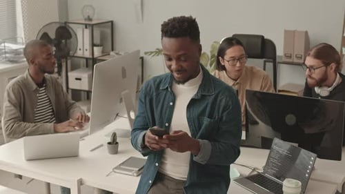 African American Programmer Texting on Smartphone at Workplace