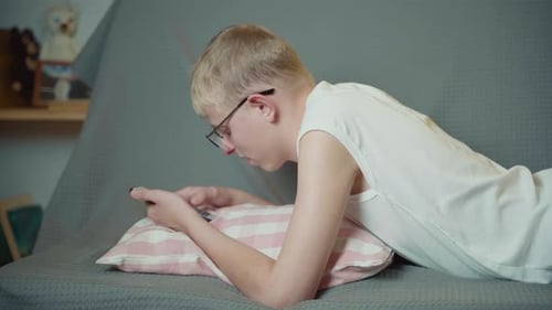 Teen Using Smartphone Lying on Couch Indoors