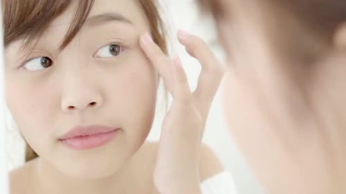 Woman Looking in Mirror Applying Skincare