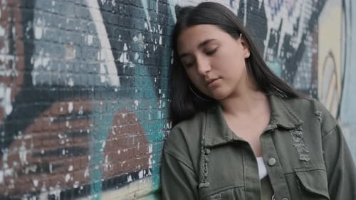 Portrait of a Young Sad Brunette Hipster Girl with Brown Eyes Near a Wall with Graffiti