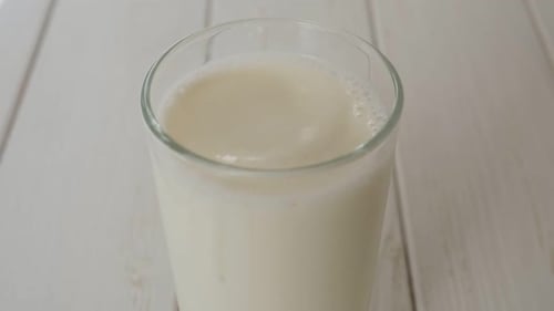 Closeup of a Drop of Milk Falling Into a Full Glass of Milk on Wooden Background