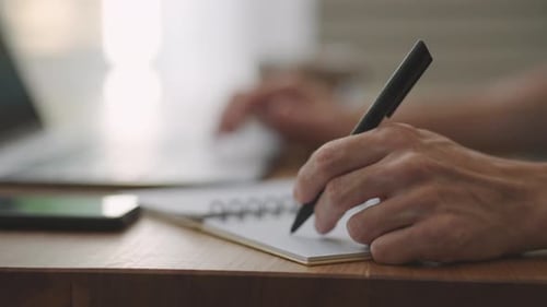 Hand Writes in Notebook at a Desk
