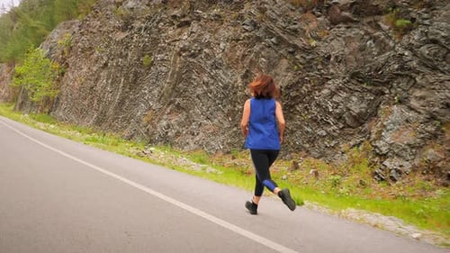 Woman Jogging on Road Next to Rocky Mountain