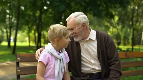 Senior Man and Grandson Talking on Park Bench