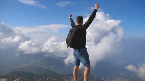 Young Male Hiker Reaching Up Top of Mountain and Raising Arms. Man Enjoying Freedom During Summer