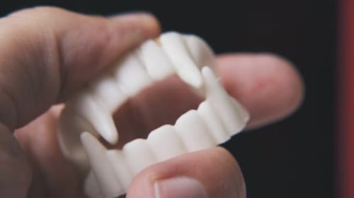 Person Plays with Funny Vampire Teeth on Black Background