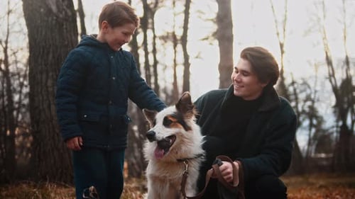 Young Man and His Little Brother Petting Their Dog in Autumn Park