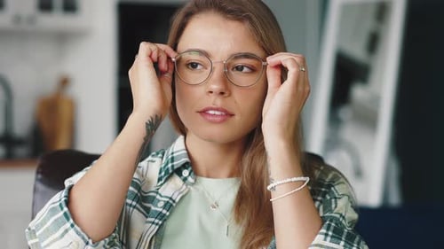 Close Up of Positive Young Blonde Woman Putting on Eyeglasses and Smiling to Camera Sitting at Home