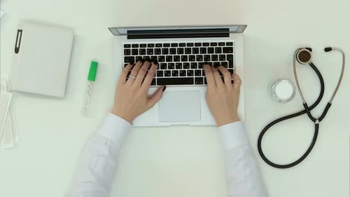 Overhead Shot of Typing on Laptop with Medical Tools