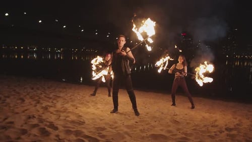 Fire Performers Twirling Flaming Staffs on Beach at Night