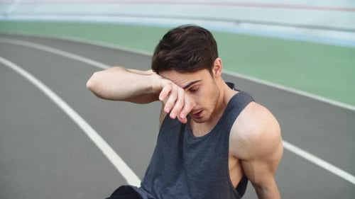 Close Up of Tired Runner Sitting on Track After Running Workout