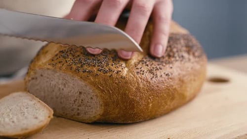 Close up of hands of woman cutting fresh bread at the kitchen. Shot with RED helium camera in 4K.
