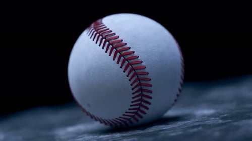 Closeup on professional white leather baseball ball on a dark background.