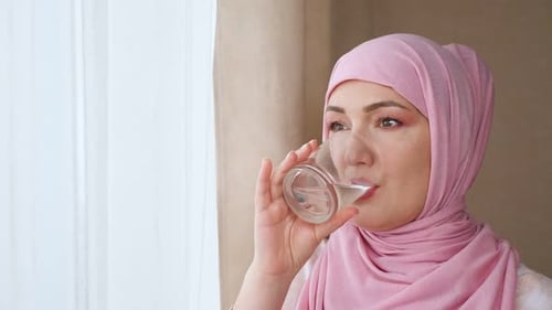 Young Woman in Hijab Drinks Water From a Glass