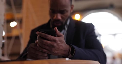 Serious African Businessman Using Smartphone Sitting in Cafe