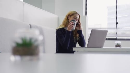 Woman on Phone Working on Laptop in Office