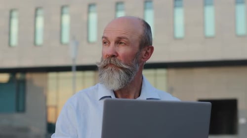 Nachdenklicher älterer Mann mit grauem Bart Kreativer Profi arbeitet am Laptop im Freien Blick zur Seite
