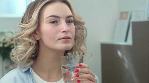 Wunderschöne junge Frau hält sich gesund, indem sie drinnen ein Glas Wasser trinkt und lächelt