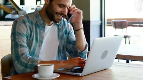 Man Working on Laptop While Talking on Phone
