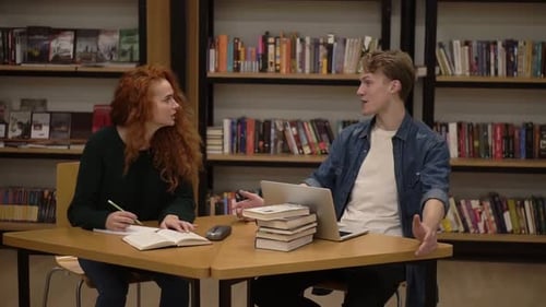 Young Male and Female Students Talking Using Laptop Explaining Course Work Study Together in Library