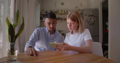 Father and Teen Daughter Using Smartphone Together Indoors