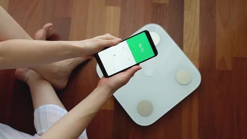 Crop woman using digital weight scales and smartphone application