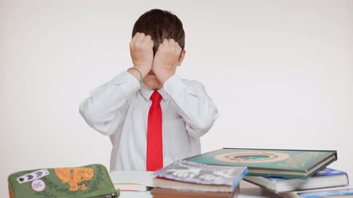 Exciting Young School Kid in Red Tie Folding Pages of Books Sitting at Table on White Background