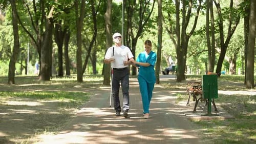Junge Krankenschwester hält blinden alten Patienten beim Gehen im Park, Klinik zur Wiederherstellung der Sehkraft