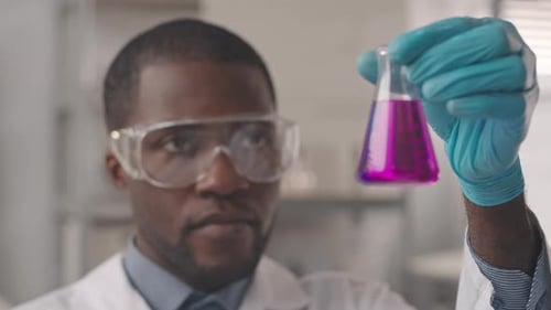 Adult Man Examines Pink Fluid in Flask