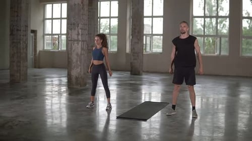 Young Man and Woman with Dreadlocks are Workouting at Empty Studio Doing Synchronous Squats Together