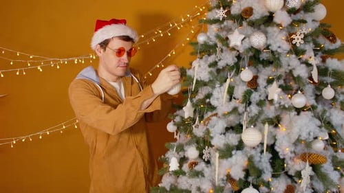 Man Decorating Christmas Tree in Santa Hat Indoors
