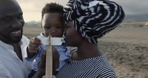 African parents and little son having fun with wood airplane on the beach