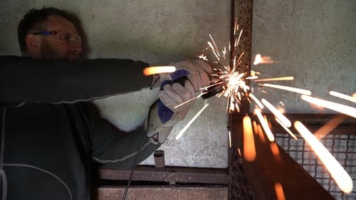 Worker using a grinder cuts metal in a workshop