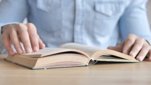 Man Turns Pages of a Book on Table