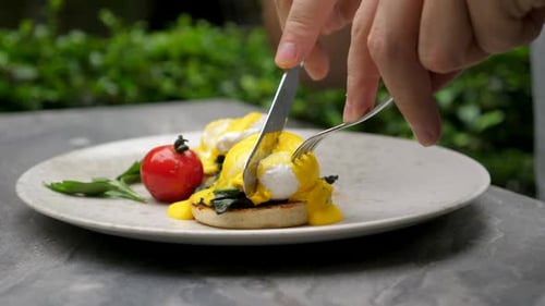 Man Eating Delicious Poached Eggs with Liquid Egg Yolk in Green Outdoor Cafe