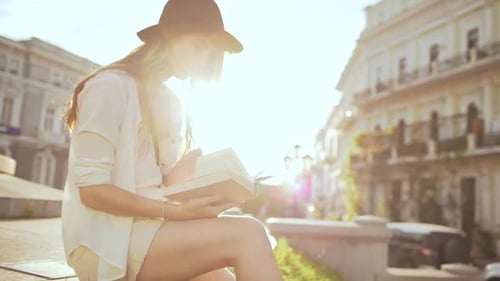 Young Beautiful Girl in Hat Reading Book in City Park