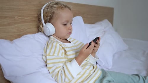 Child Using Smartphone With Headphones on Bed
