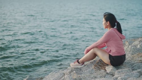 Woman Sitting Calmly on Rocks Overlooking the Ocean