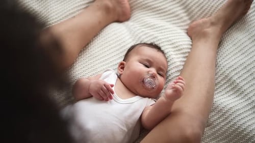 Closeup View of Mom Stroking Cute Baby and Lying on Bed in Home Bedroom Indoors Spbd