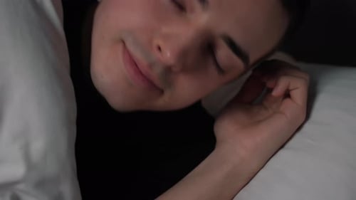 Un bel homme calme et souriant s'endort dans un lit confortable et frais, profitant d'une bonne sieste de sommeil