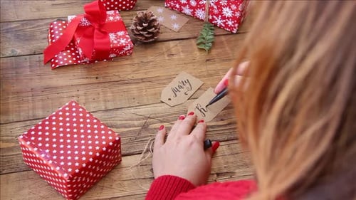 Woman Hand Writing Holiday Gift Tags at Wooden Table