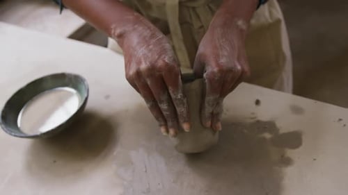 Close up view of female potter wearing apron working on clay to create pot at pottery studio
